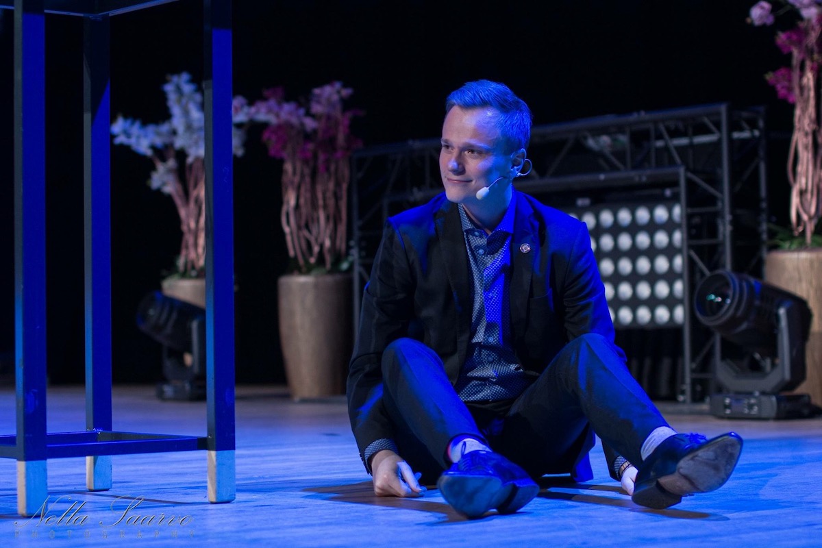 Henri mustassa puvussa istuu lattialla teatterilavalla sinisen valon alla.